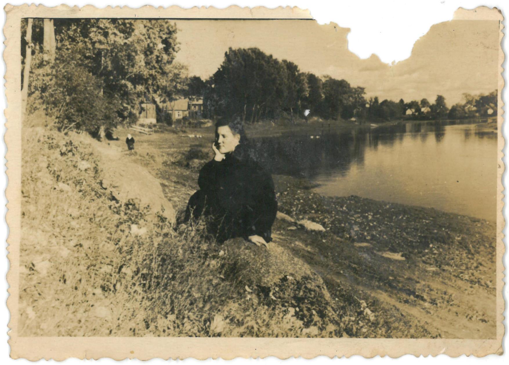 Neatpažinta moteris sėdi ant akmens prie Lėvens upės, ties Kalno gatve, Pasvalyje