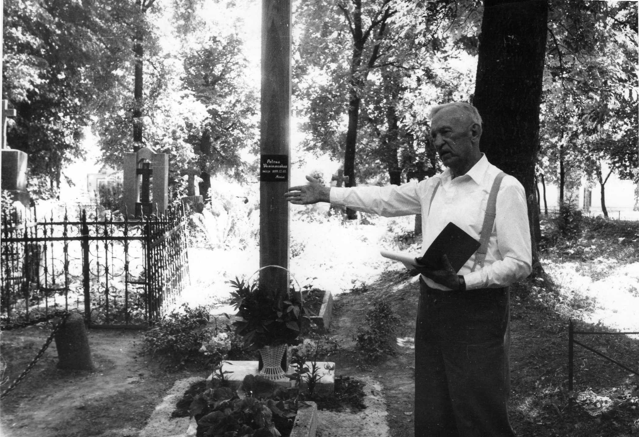 Profesorius, agronomas Petras Vasinauskas prie prosenelio Petro Vasinausko kapo. 1989 m. Kapą puošia medinis kryžius. Užrašas ant kryžiaus: „Petras Vasinauskas miręs 1899 12 09. Ainiai“ 